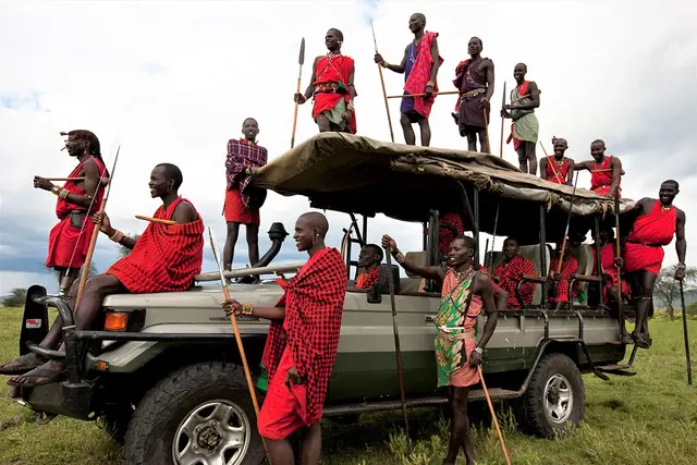 Maasai hosts riding out on a safari vehicle